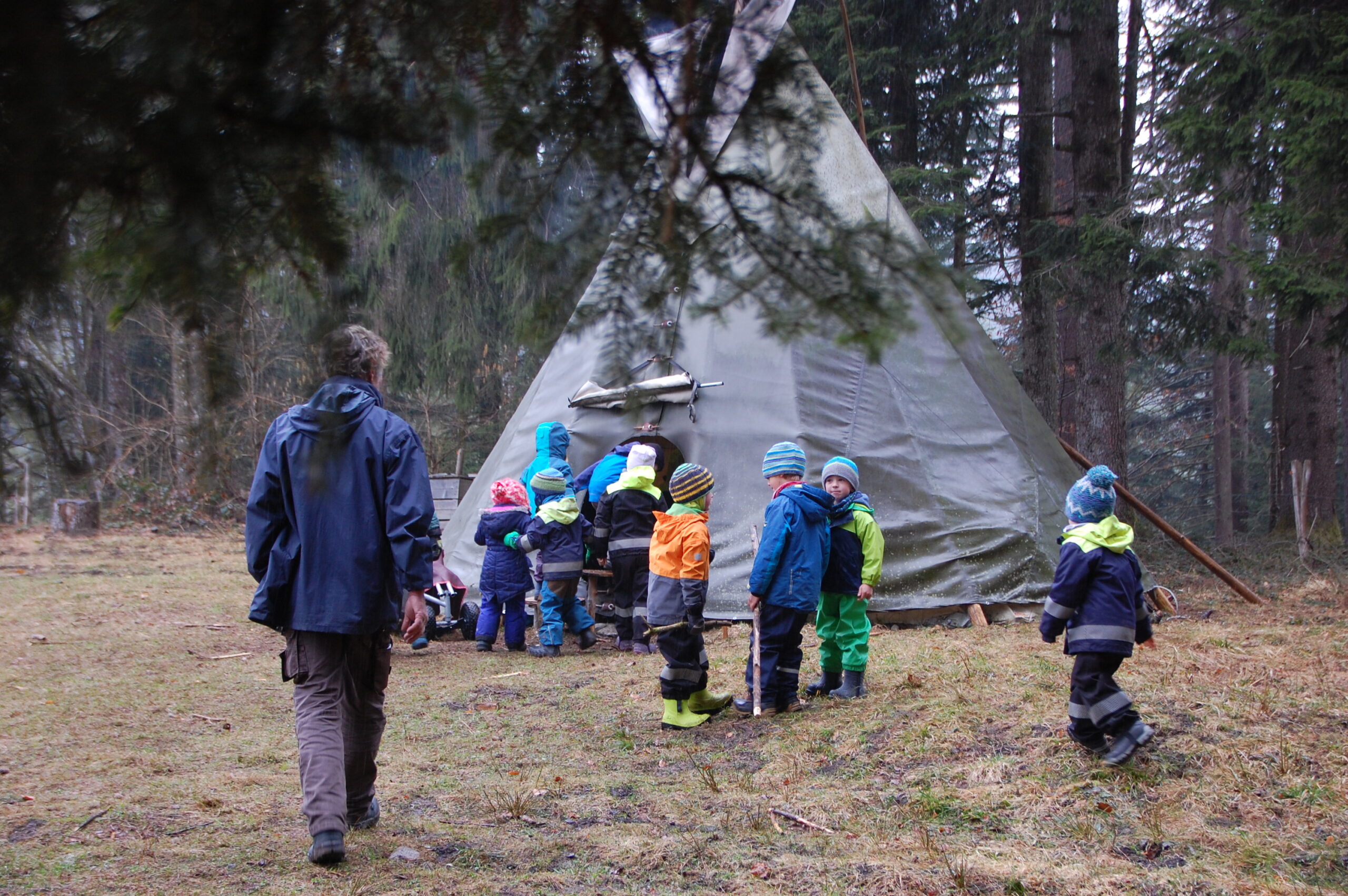 einige Kinder und ein erwachsener in herbstlichen Outfits vor einer großen Jurte auf einer Freifläche umringt von Nadelbäumen