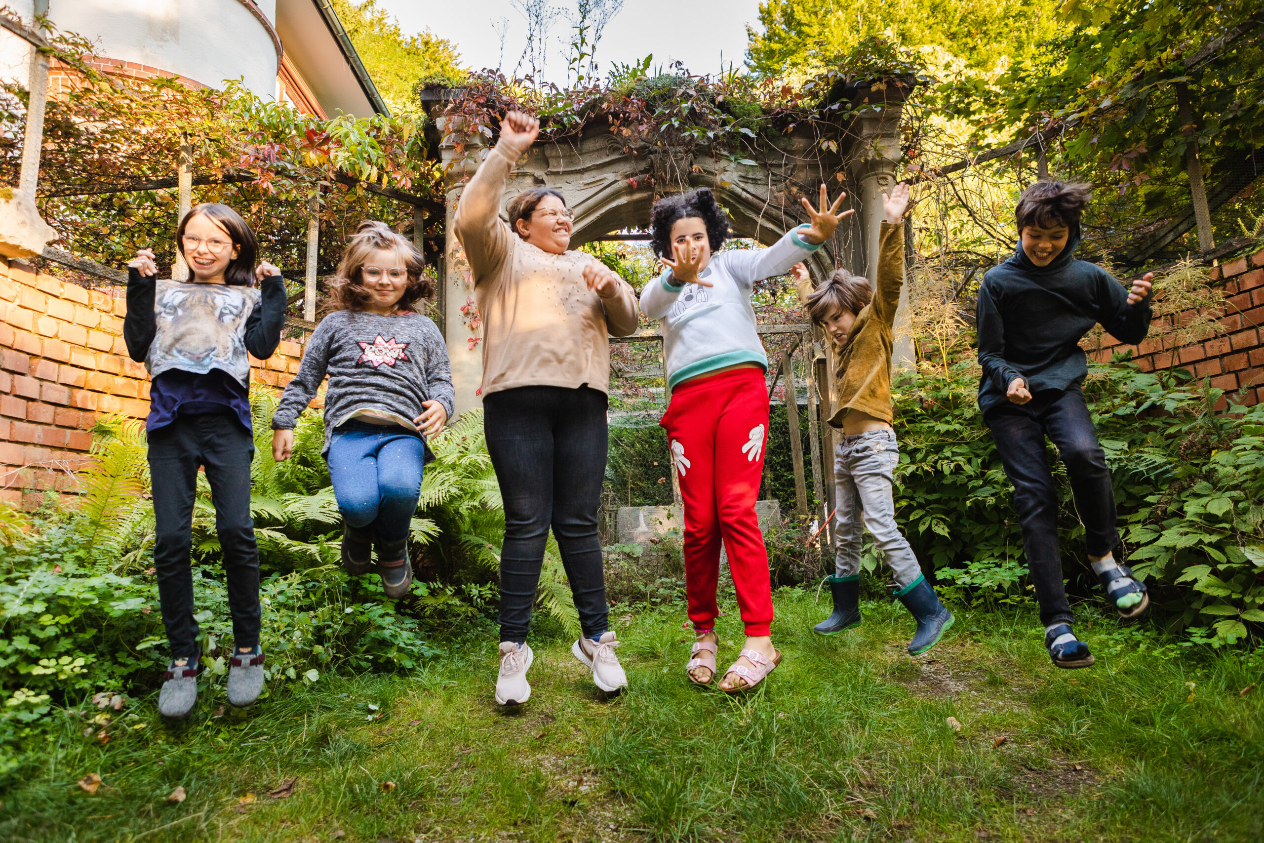 6 Kinder, 4 Mädchern und 2 Jungen, die in die Luft springen und dabei Grimassen schneiden.